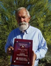Steve Husman is pictured outdoors holding an award plaque.