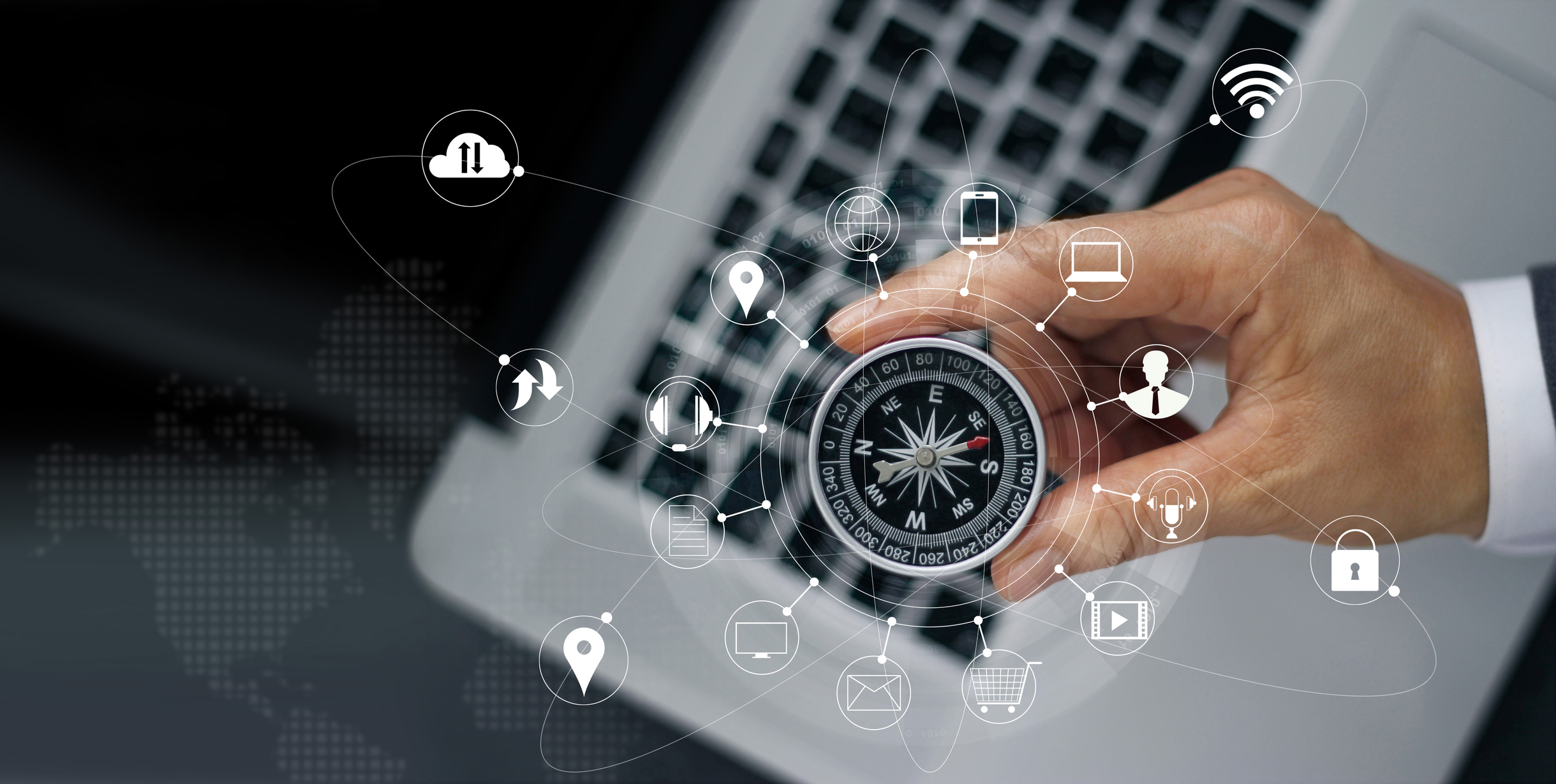 A compass held in a person's hand with a computer keyboard in the background.