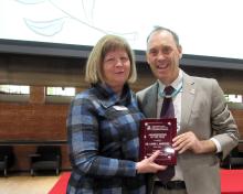 Award recipient pictured on stage with plaque, standing next to award presenter.