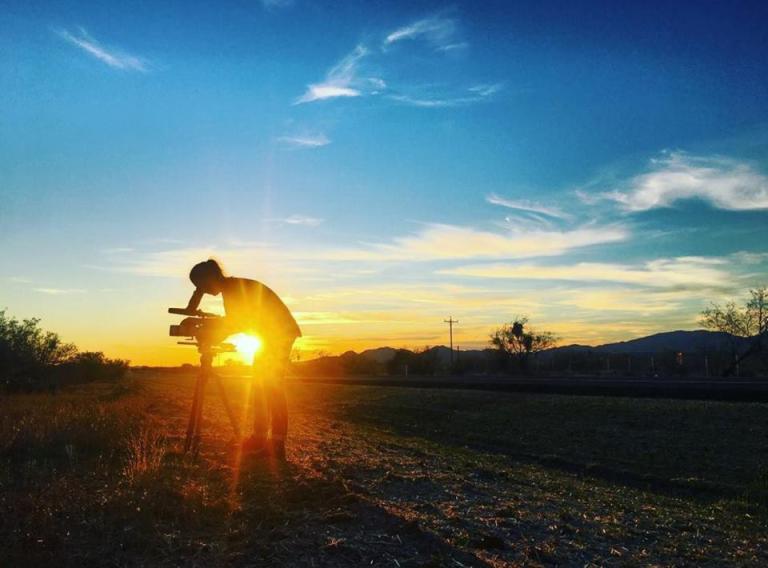 Sandra Westdahl setting up a video camera outside with sunset in the background.